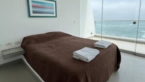 A bedroom with a bed, a framed picture on the wall, and a view of the sea through large windows. - Terrace with Jacuzzi, Duplex, Ocean View, Grill (Punta Hermosa)