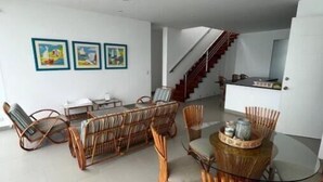 A modern living room with a glass dining table surrounded by wicker chairs, a staircase leading to a kitchen, and framed artwork on the wall. - Terrace with Jacuzzi, Duplex, Ocean View, Grill (Punta Hermosa)