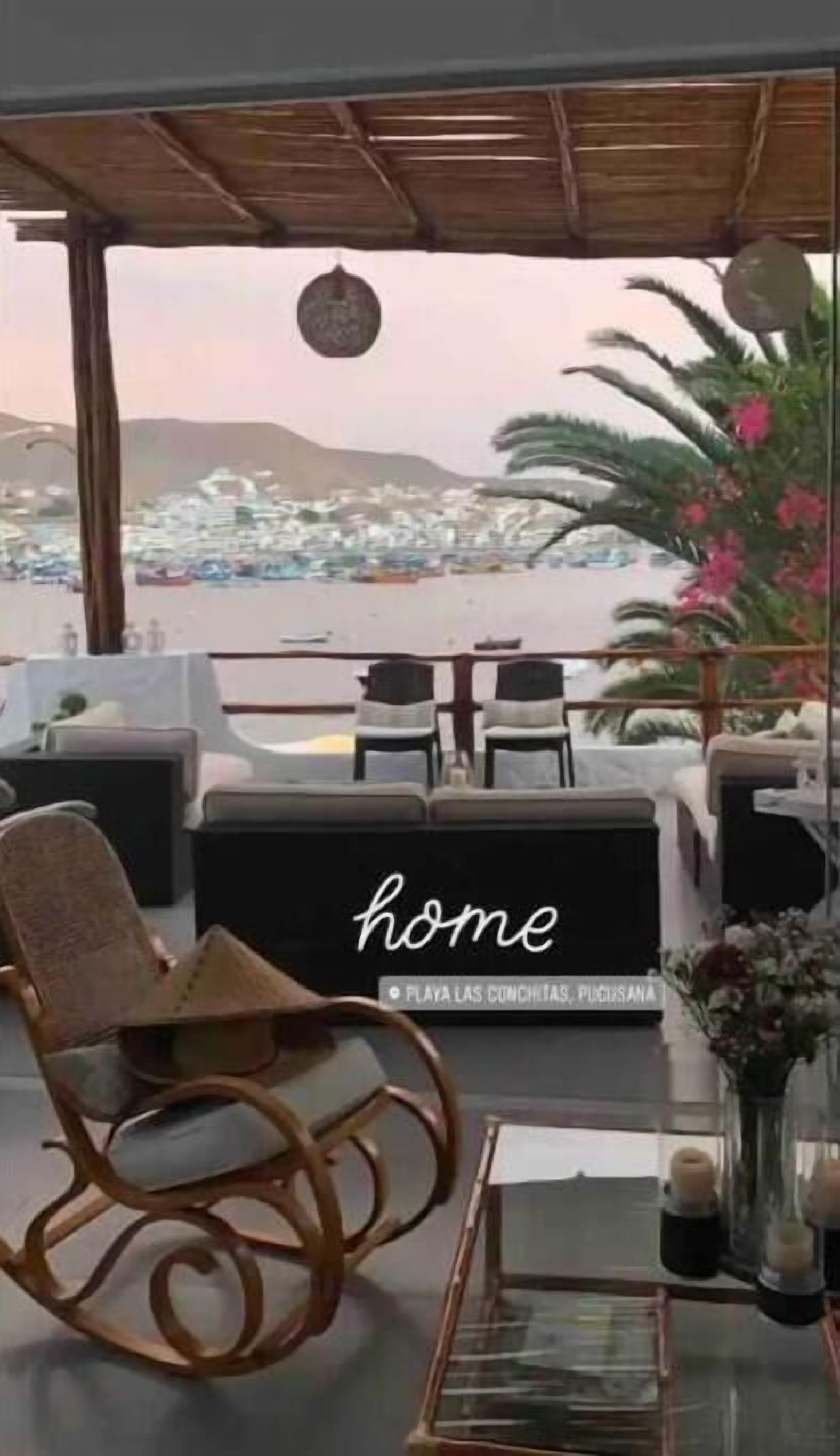 Un espacio de relax frente a la playa con sillas de mimbre y una mesa de vidrio, con vistas a un pueblo costero.