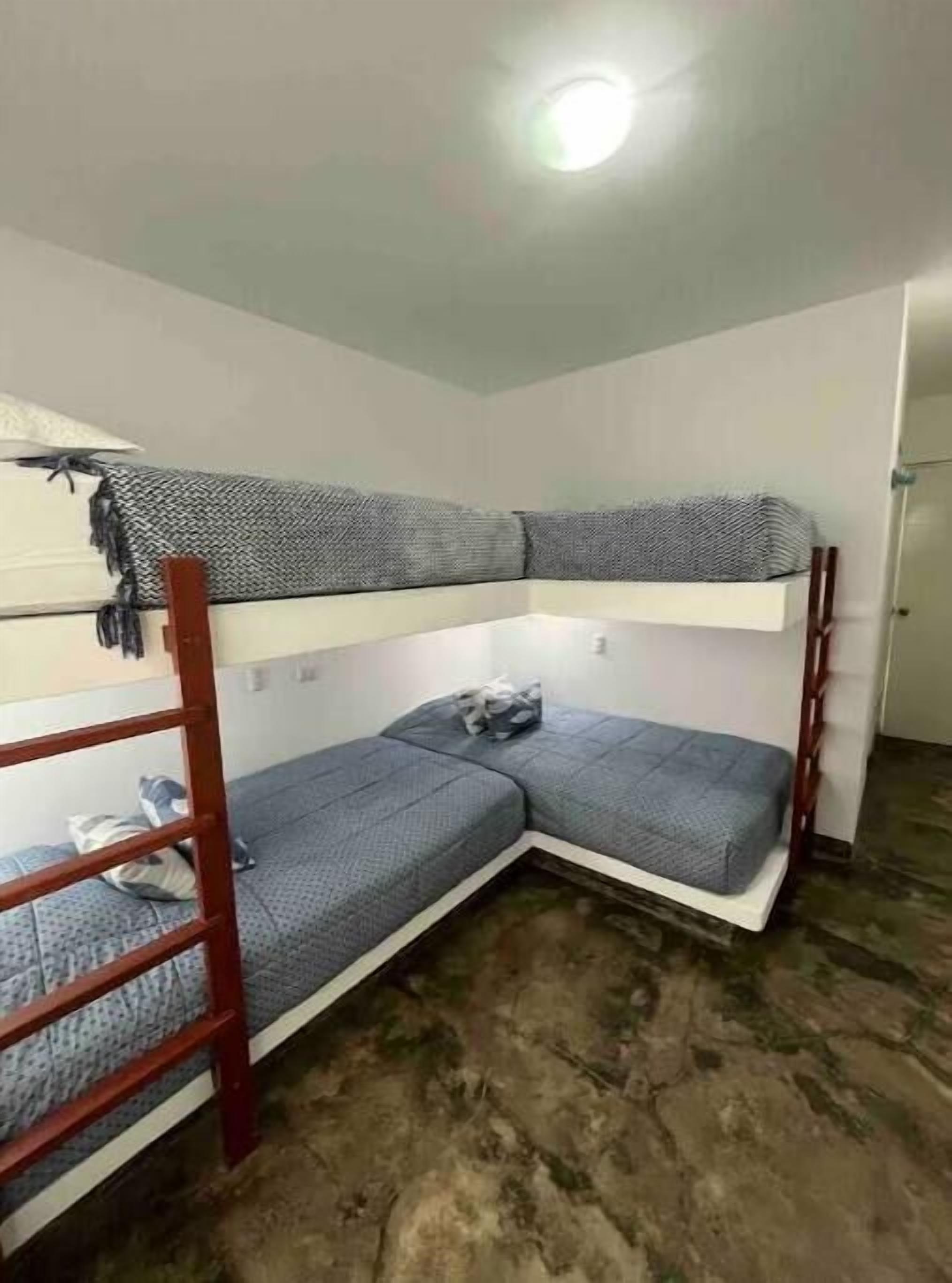 A bunk bed room with a wooden frame, a white wall, and a ceiling light.