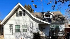 A single-story house with a gabled roof, a small attached garage, and a front yard with a lawn and a tree. - Sunset Melody - pet friendly  (Amarillo)