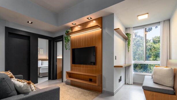 A modern living room with a flat-screen TV, wooden entertainment unit, and a cozy seating area with a cushioned bench. - 5 Minutes From Leblon Beach Ap302 (Rio de Janeiro)