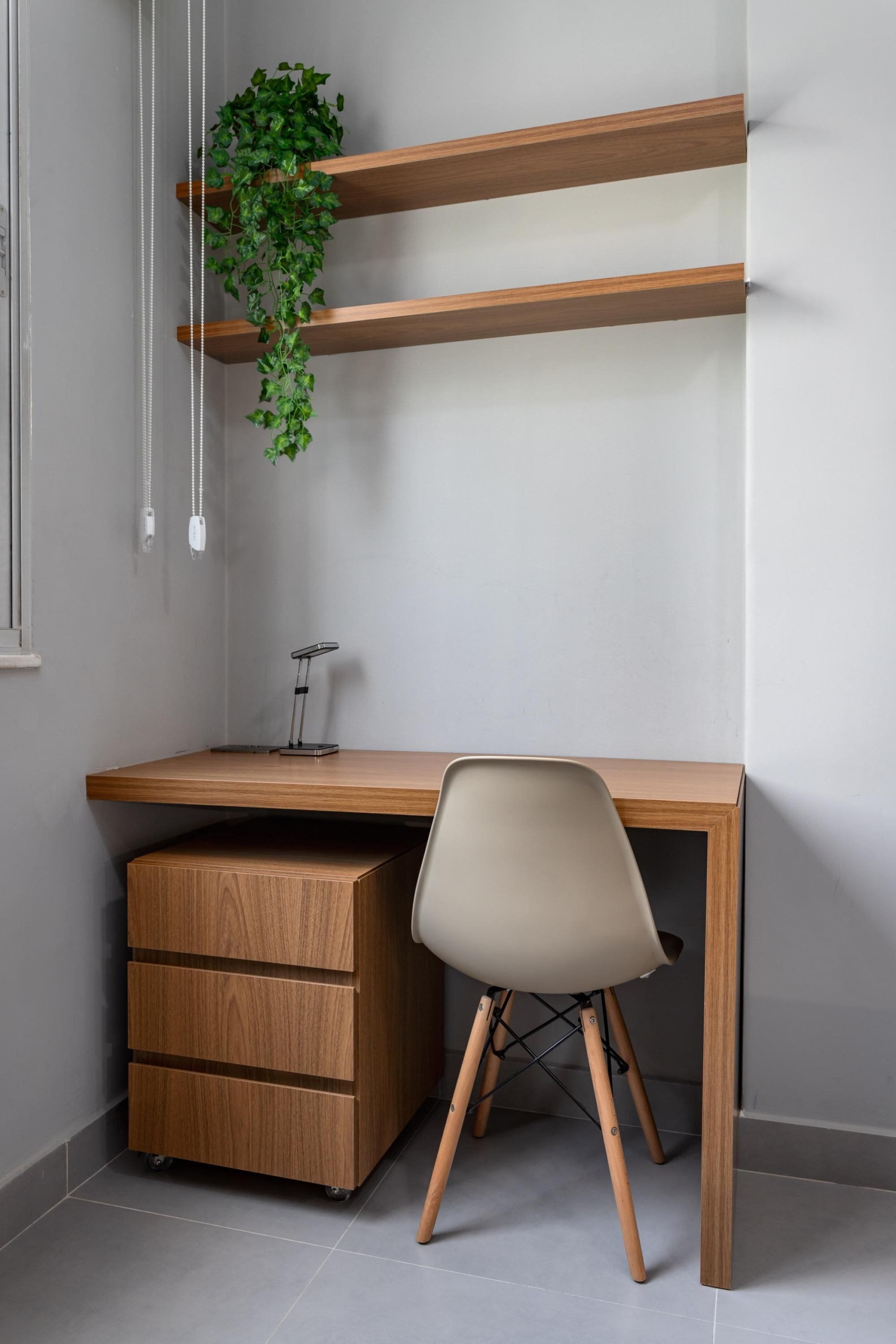 Uma mesa moderna com acabamento em madeira, uma cadeira branca e uma pequena planta em uma estante.