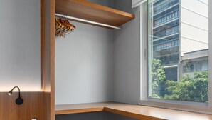 A corner bedroom with built-in wooden shelving, a small stool, and a window with a view of buildings and greenery. - 5 Minutes From Leblon Beach Ap302 (Rio de Janeiro)