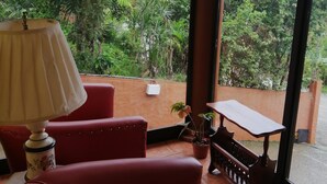 A room with a red sofa, a table, and a lamp. There is a view of greenery outside through large windows. - Hotel SantaFe Monteverde  (Monteverde)