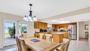 A modern kitchen with wooden cabinets, stainless steel appliances, and a dining area with a large table and chairs. - Perfect for Families, Friends and Budget of all Sizes! Great Deal! Heated Pool! (Cape Coral)