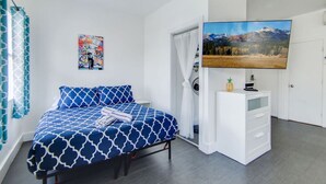 A bedroom with a bed, a television, a white dresser, and a painting on the wall.