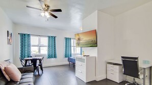 A modern living room with a sofa, a dining table, a white desk, and a ceiling fan.