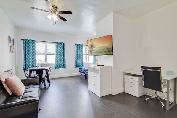 A modern living room with a sofa, a dining table, a white desk, and a ceiling fan.