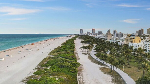 A coastal cityscape with a wide beach, a promenade lined with palm trees, and high-rise buildings in the background.