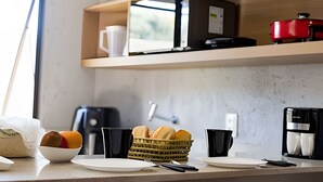 A kitchen counter with a basket of bread, a coffee maker, and a red pot on the shelf above.