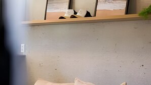 A beige sofa with wooden legs, a white cushion, and a shelf above holding two framed pictures of a beach scene.