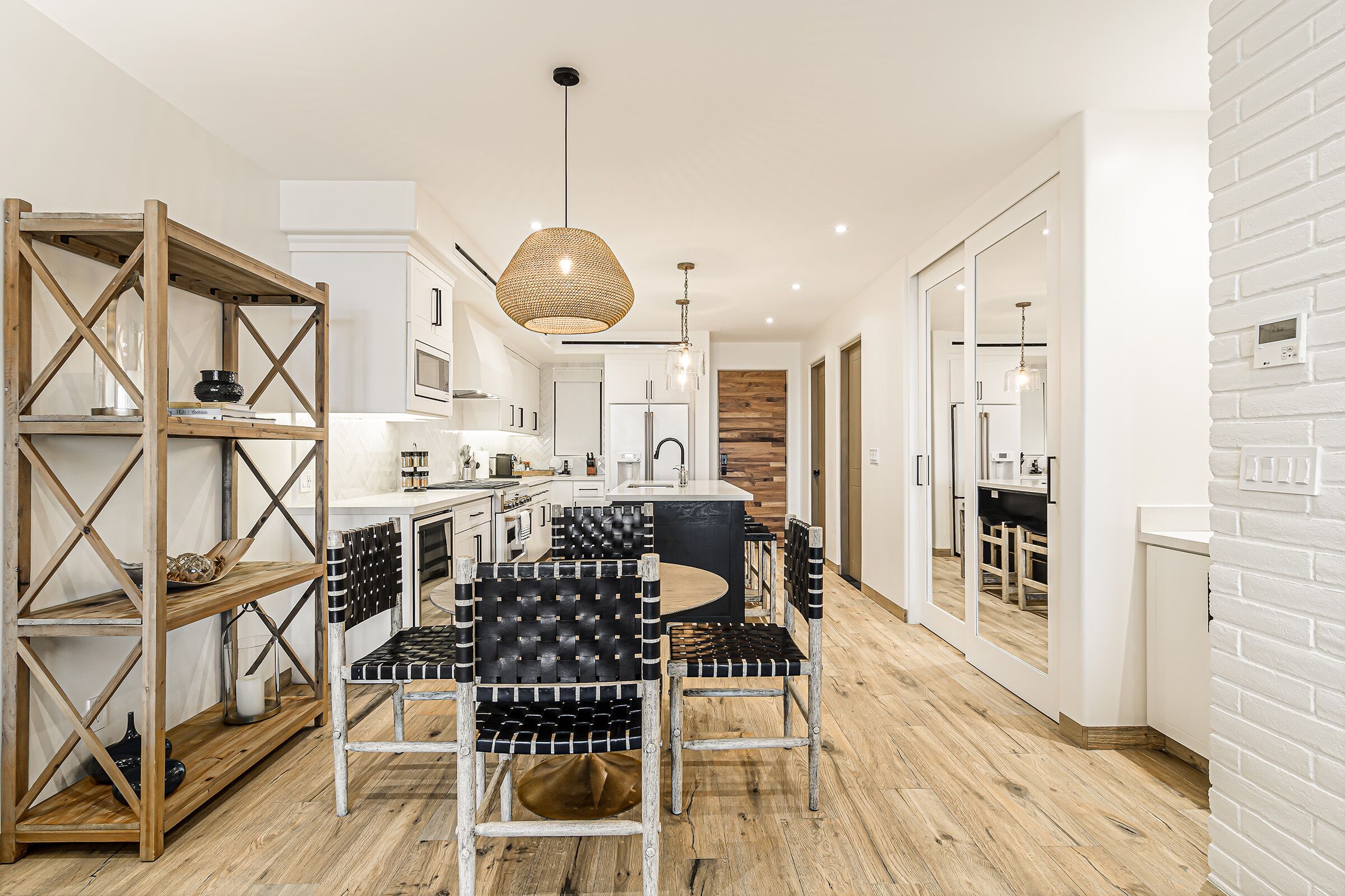 A modern kitchen with white cabinetry, a wooden dining table, and black cushioned chairs.