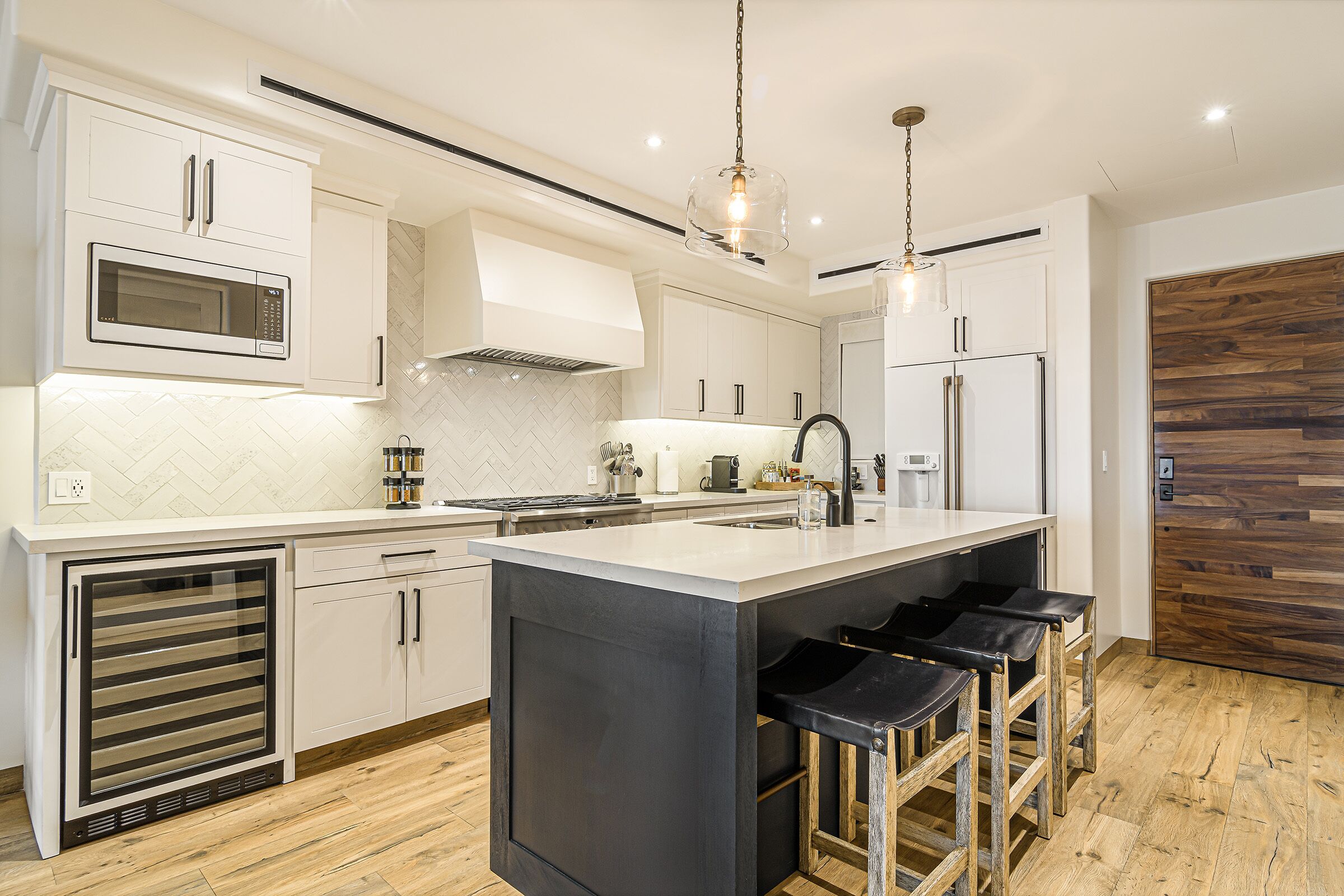 A modern kitchen with white cabinetry, a central island with bar stools, a microwave, and a refrigerator.