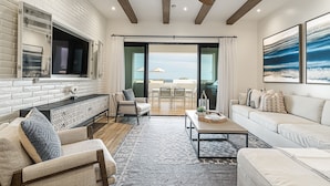 A modern living room with a fireplace, a large TV, and a dining area with a view. - Beachfront Flats (San José del Cabo)