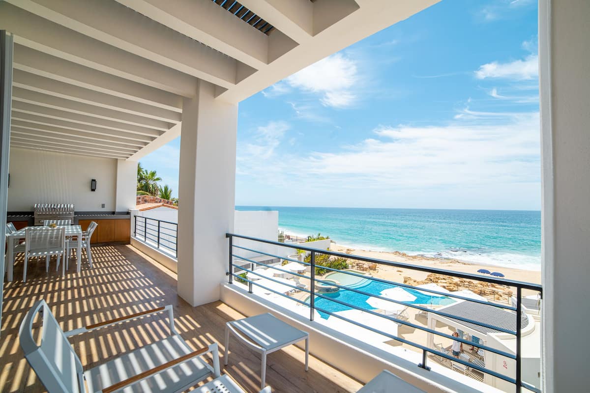 A balcony with a view of the beach and ocean, a pool, and outdoor seating.