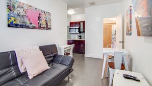 A modern living room with a black leather sofa, a white dining table, and a kitchen in the background. - Comfy 1 B/R, Near Ocean Dr & Beach - South Beach (Miami Beach)