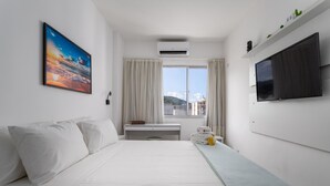 Ein Hotelzimmer mit einem großen Bett, einem Schreibtisch, einem Flachbildfernseher und einem Fenster mit Vorhängen.