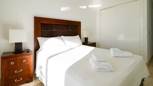 Una cama bien hecha con sábanas blancas y dos toallas dobladas al lado.
