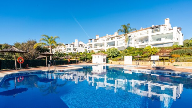 Una piscina con agua cristalina azul, rodeada de sombrillas y una pequeña zona junto a la piscina.