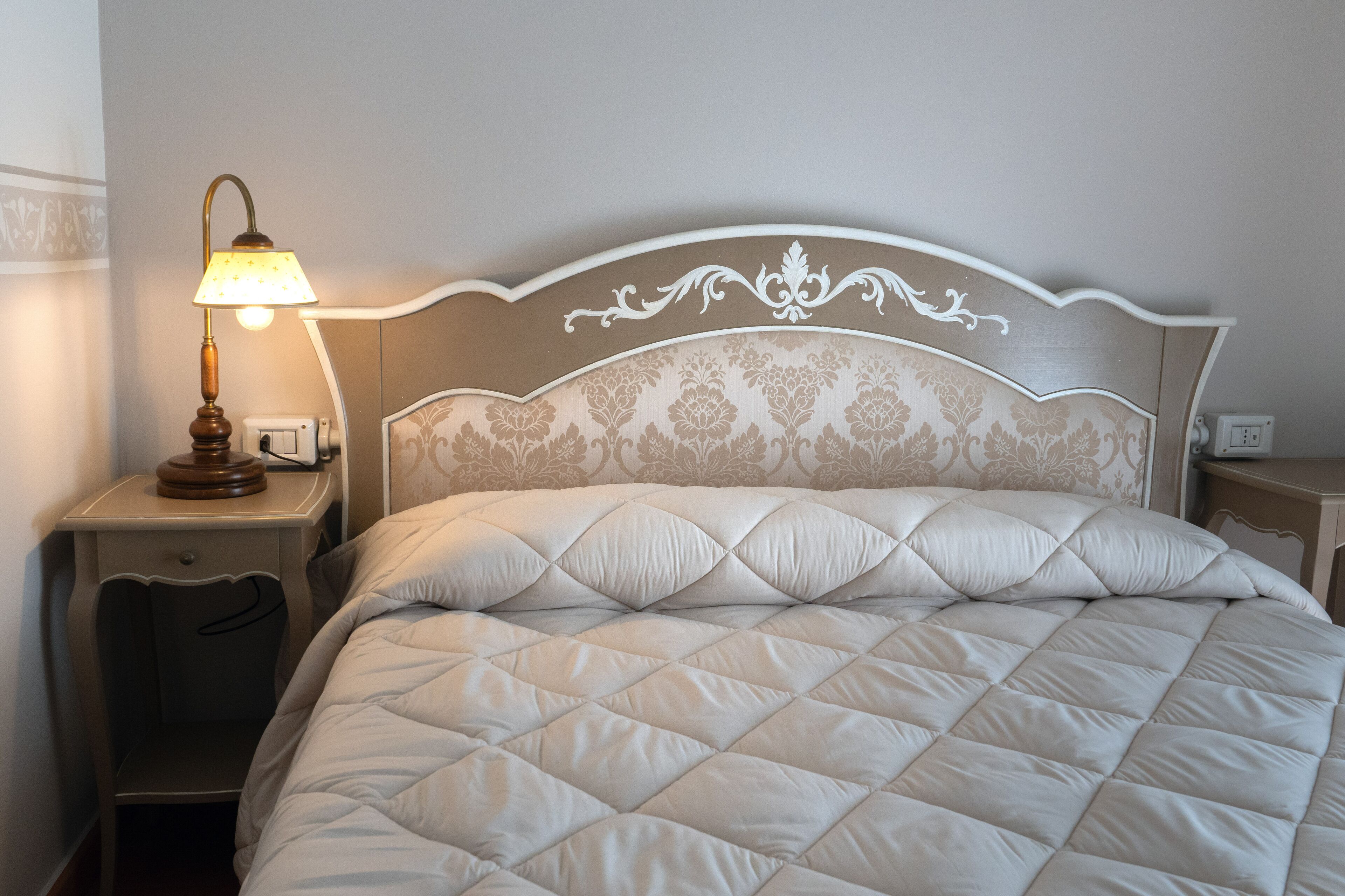 Una cama bien hecha con un cabecero acolchado, una lámpara de noche y una mesita de noche con cajón.