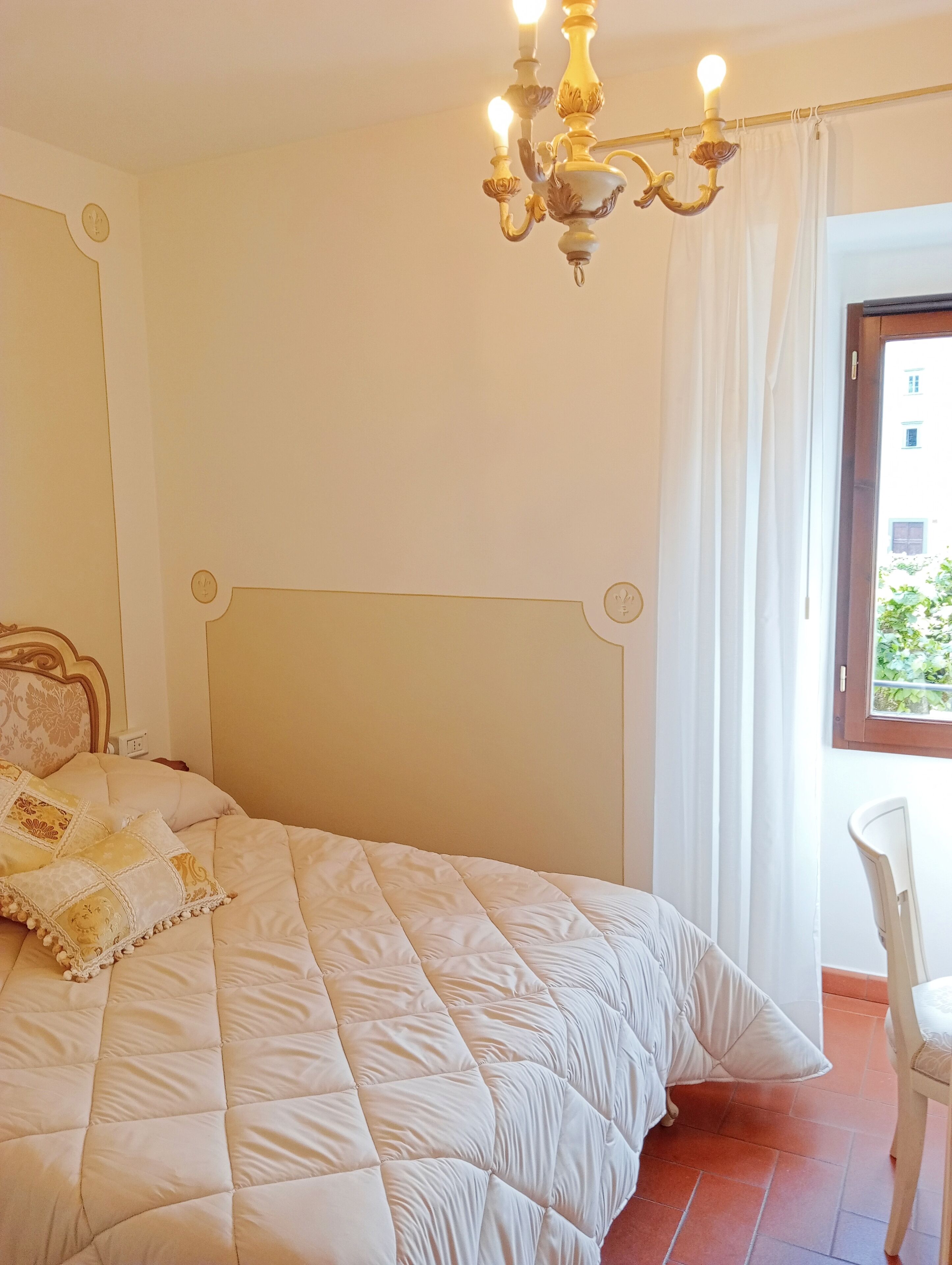 Een slaapkamer met een bed, een kroonluchter, een raam met gordijnen en een stoel.