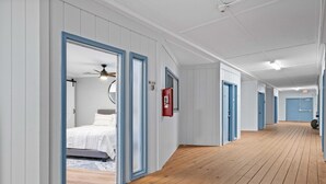 Un pasillo de hotel con suelo de madera, paredes blancas con detalles azules y puertas que dan a las habitaciones.