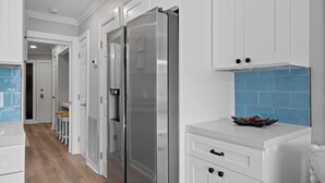 Una cocina moderna con armarios blancos, un refrigerador de acero inoxidable y un salpicadero de azulejos azules.