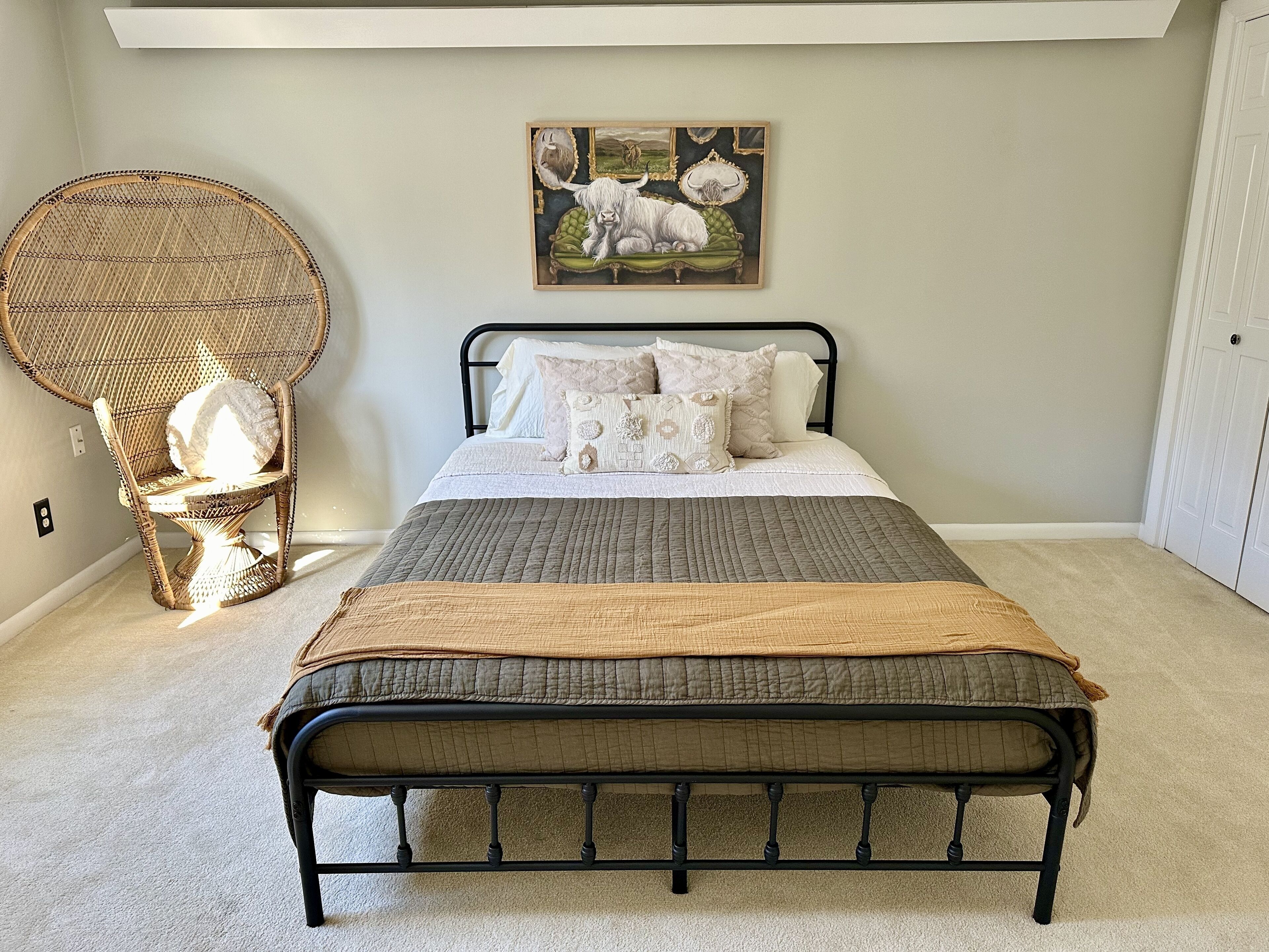 Une chambre à coucher avec un lit, une chaise en osier et un tableau accroché au mur.