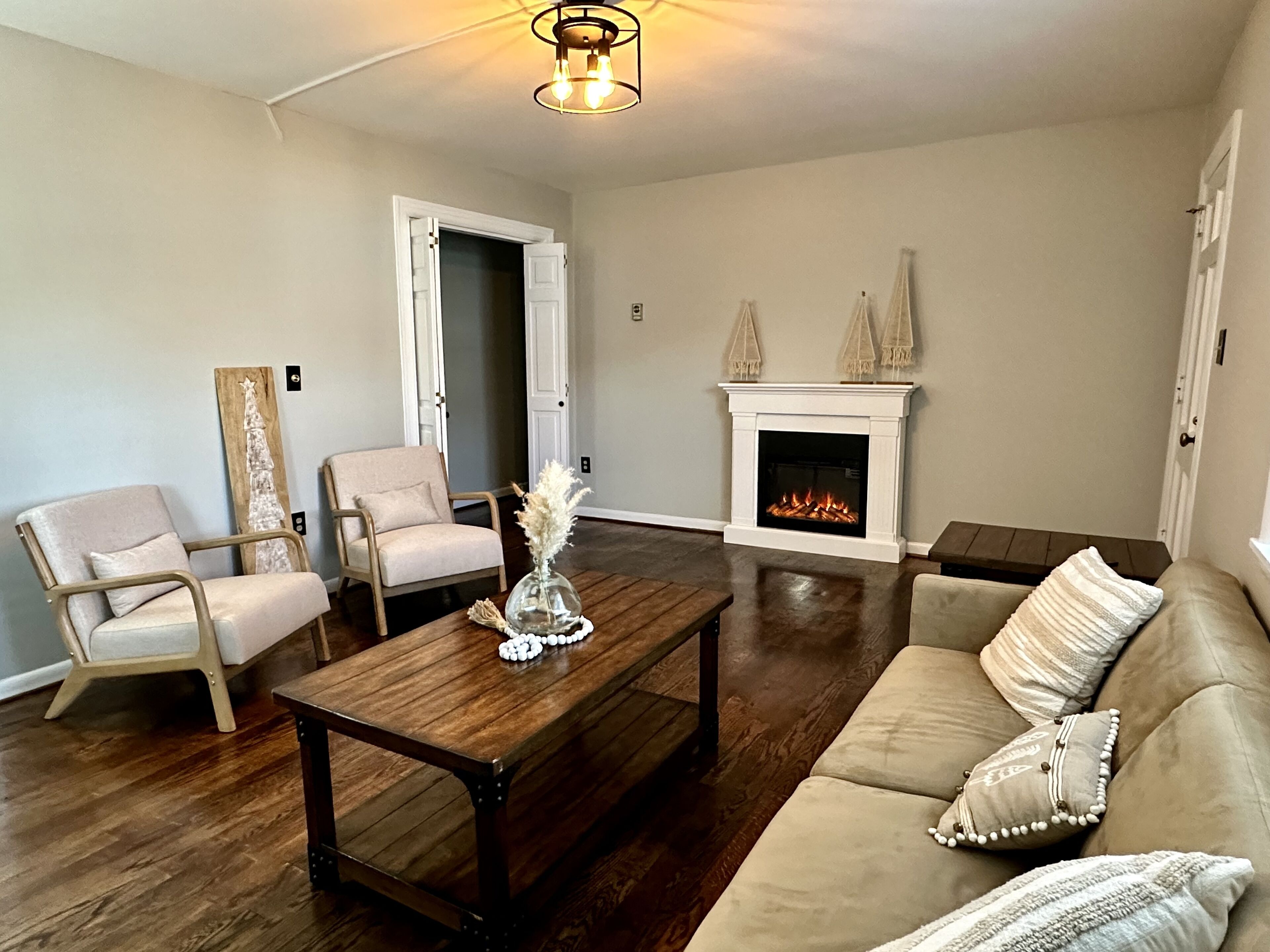 Una sala de estar con chimenea, dos sillones, una mesa de centro de madera y un sofá.