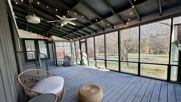 A covered outdoor deck with wicker furniture, a ceiling fan, and string lights.