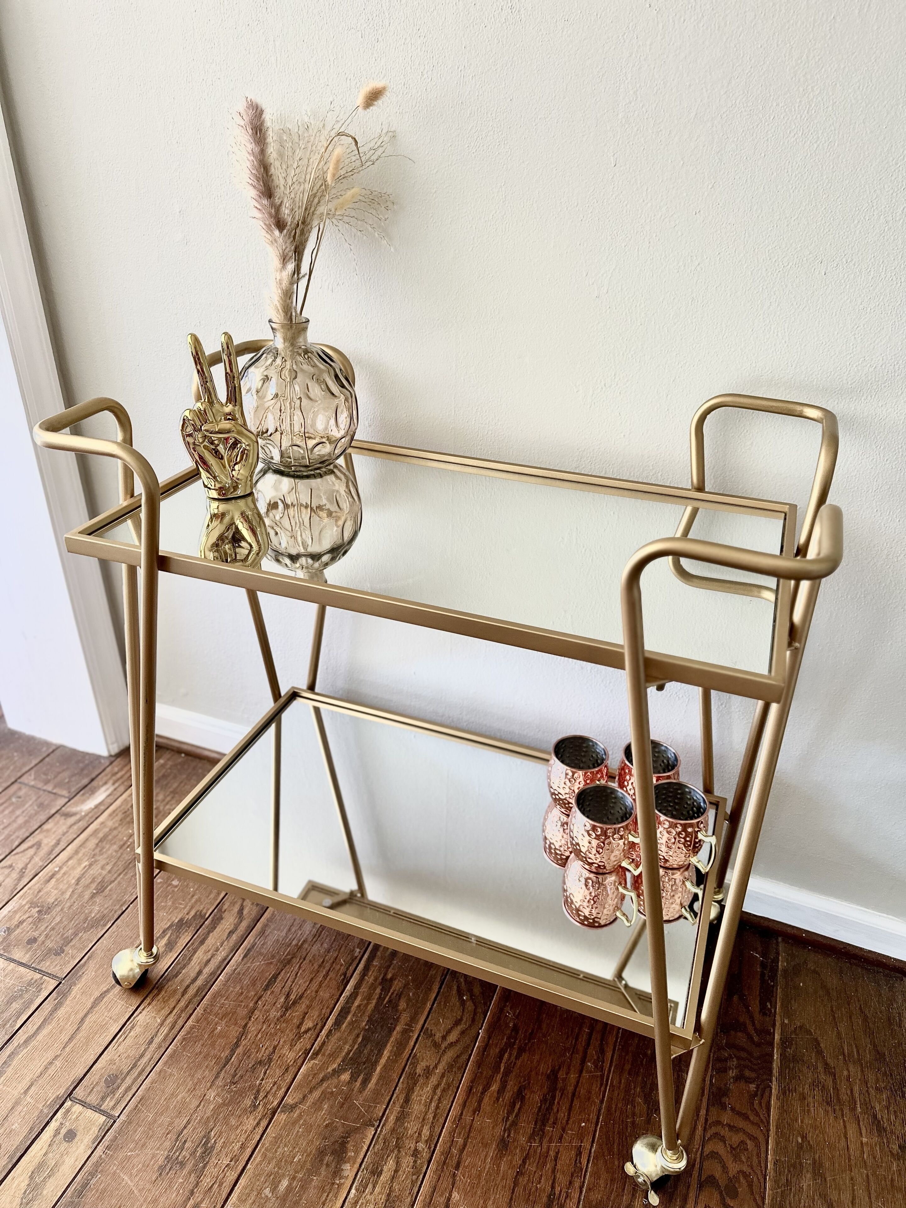 A gold metal shelf with decorative items and a vase against a white wall.