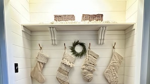 A corner with a wooden bench, three knitted stockings, a wreath, and a small shelf with decorative items.