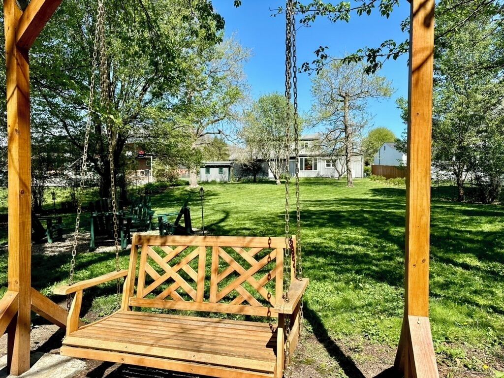 Un ensemble de balançoires en bois installé dans un espace verdoyant, avec des arbres et des maisons en arrière-plan.