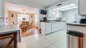 A modern kitchen with white cabinets, a dishwasher, and a microwave. There is a dining area with a wooden table and chairs. - Stylish Port Richey Home ~ 8 Mi to Beach Park! (Port Richey)