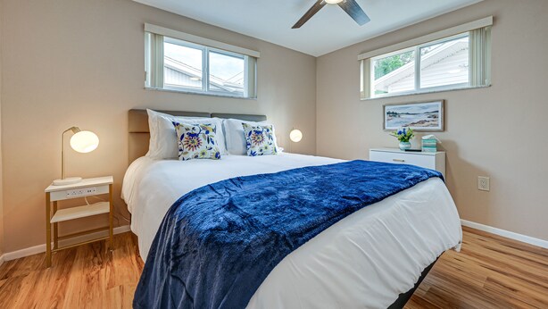 A bedroom with a bed, bedside tables, a ceiling fan, and two windows. - Stylish Port Richey Home ~ 8 Mi to Beach Park! (Port Richey)