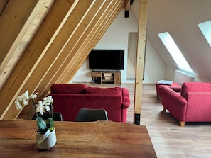 Um loft moderno com teto inclinado, vigas de madeira, um sofá vermelho, uma mesa de jantar de madeira e uma orquídea em vaso.