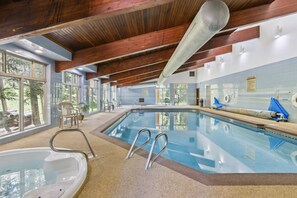 En inomhuspool med väggar av genomskinligt glas, träbjälkar och utsikt över träd utanför.