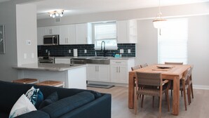 A modern kitchen with white cabinets, a black backsplash, and stainless steel appliances. There is a dining area with a wooden table and chairs.