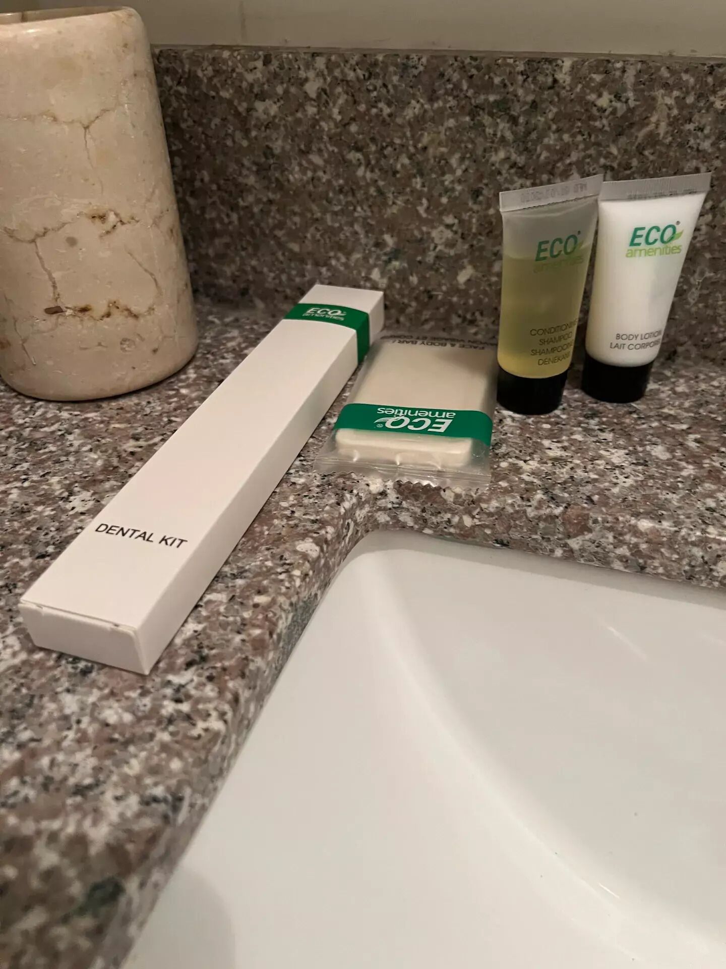 Una superfície de bany amb un estri de dentista, dues tubs de loció corporal ECO Amenities i un tub de pasta de dents.