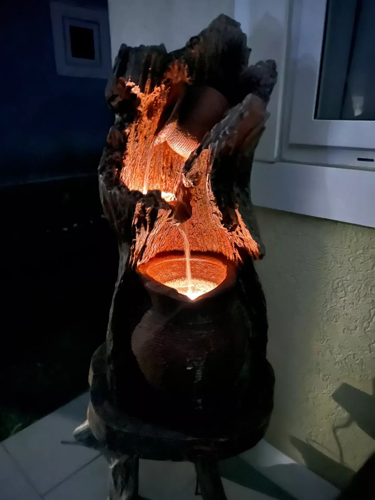 A wooden sculpture with a light source inside, placed on a tiled floor.