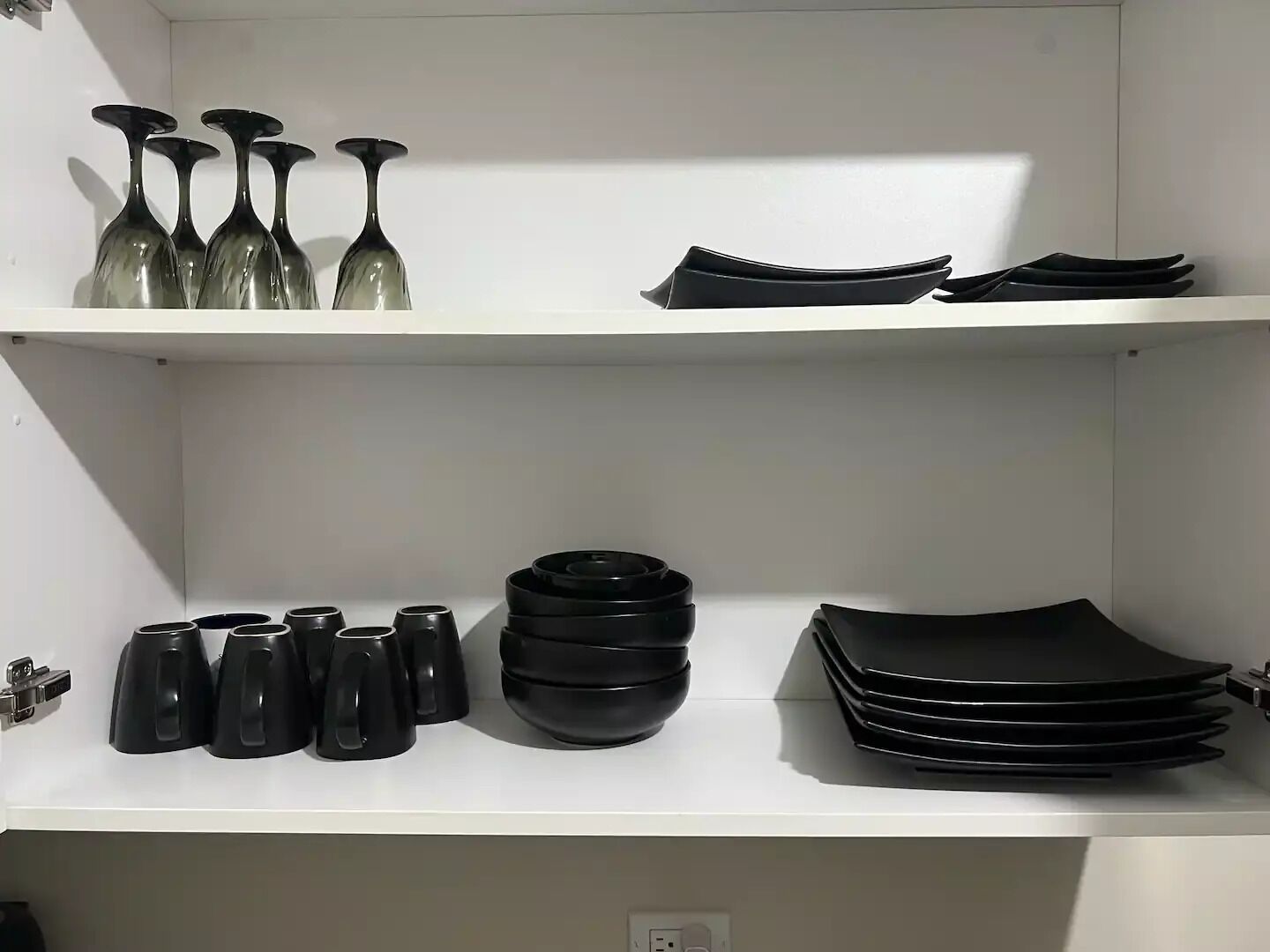 Une cuisine avec des étagères blanches où sont rangés des ustensiles de cuisine noirs, notamment des tasses, des bols et des assiettes.