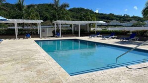 A rectangular pool with clear blue water, surrounded by a tiled deck. There are lounge chairs and a covered seating area with umbrellas. - Serenity get away @Oceanpointe 2BR 2BTHRM solar wifi (Lucea)