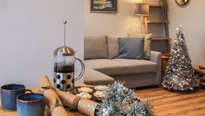 Un salon chaleureux avec un canapé, une machine à café, un petit sapin de Noël et un tableau encadré accroché au mur.