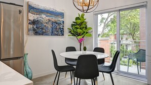 A modern kitchen with a stainless steel refrigerator, a white dining table with black chairs, a large abstract painting, and a potted plant with pink flowers. - Beautifull Penthouse 2 bedrooms/2 bathrooms condo with private terrasse. (Montréal)