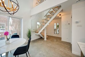 Um interior moderno com escada, área de refeições com mesa e cadeiras, e uma janela grande.