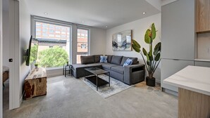 A modern living room with a grey sectional sofa, a coffee table, and a large window offering a city view. - Beautifull Penthouse 2 bedrooms/2 bathrooms condo with private terrasse. (Montréal)