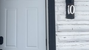 Une porte blanche avec un cadre noir, une boîte aux lettres noire et le numéro de maison « 10 » en blanc sur un mur de briques blanches.