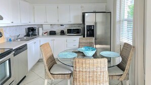 A modern kitchen with white cabinets, stainless steel appliances, and a glass dining table with wicker chairs. - Fun in the Sun (Naples)