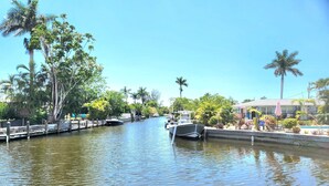 A canal with boats docked on the side, surrounded by lush greenery and palm trees. - Fun in the Sun (Naples)